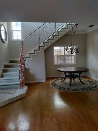 Interior view of a staircase and dining area with hardwood floors and ornate railing.