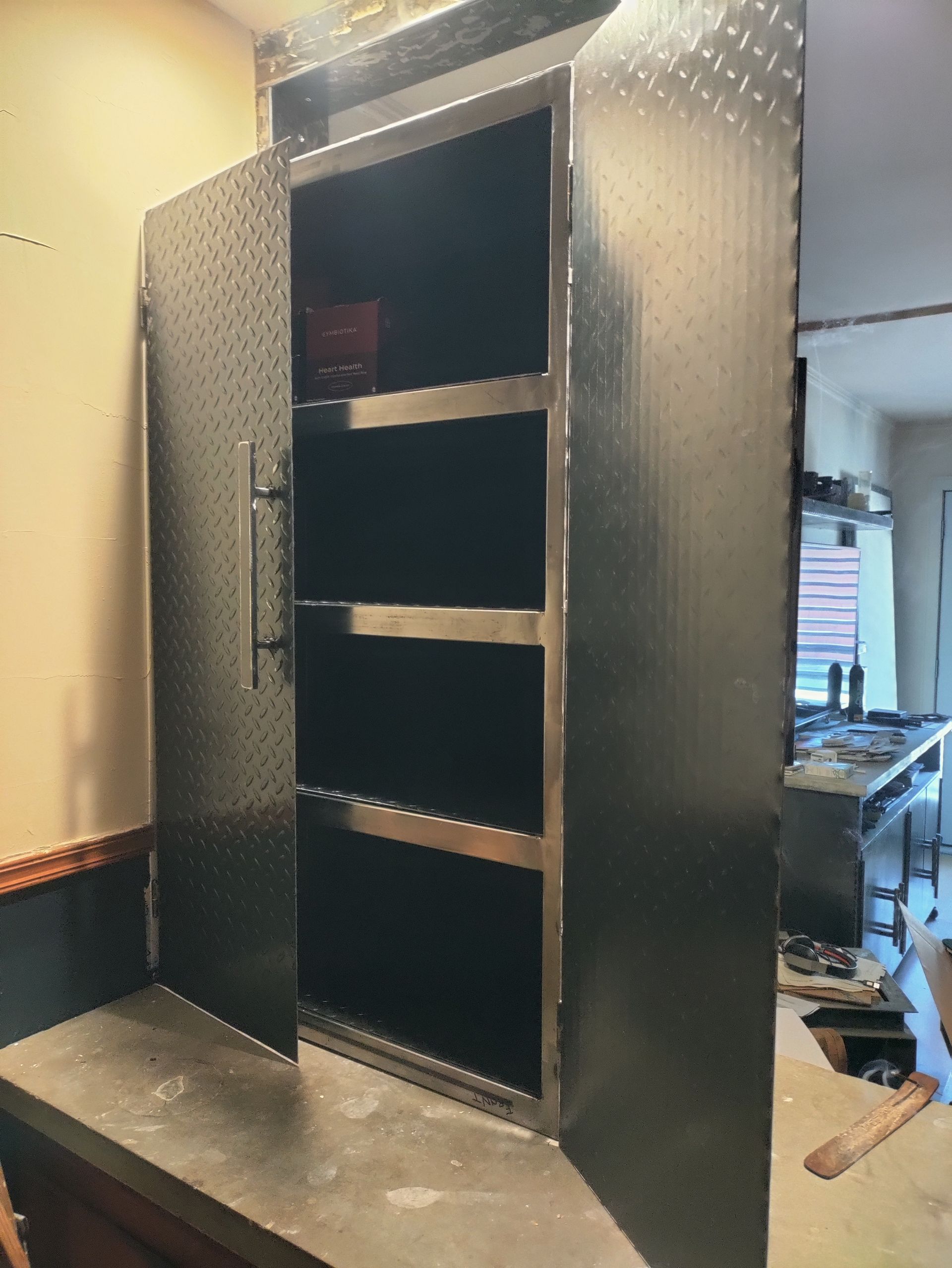 Metal cabinet with open doors, three shelves, and a handle, on a countertop. Interior is dark.