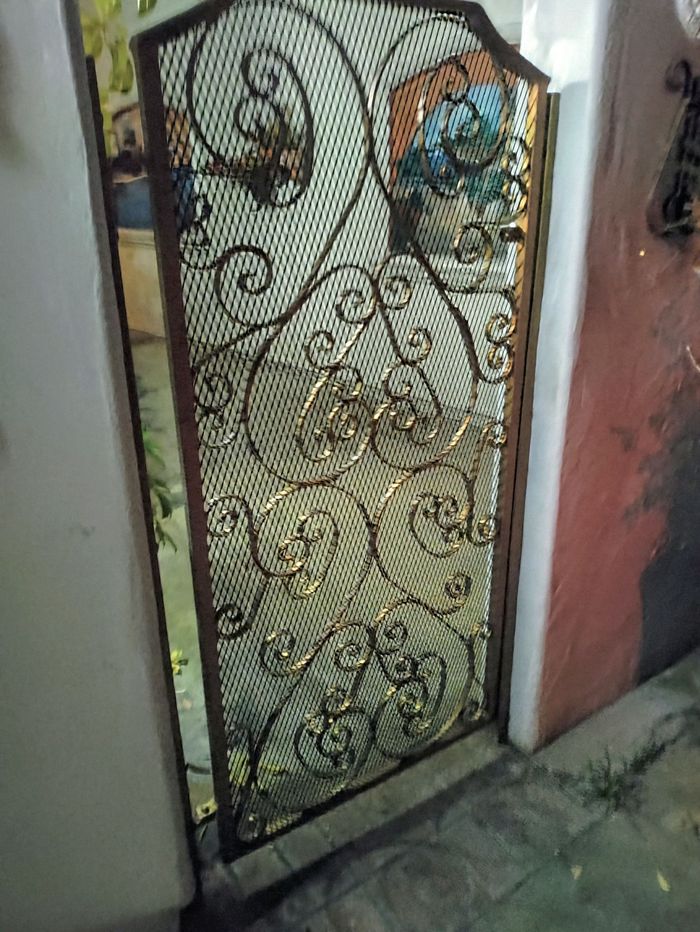 Ornate metal gate with swirling patterns, set in a doorway between white and red walls.