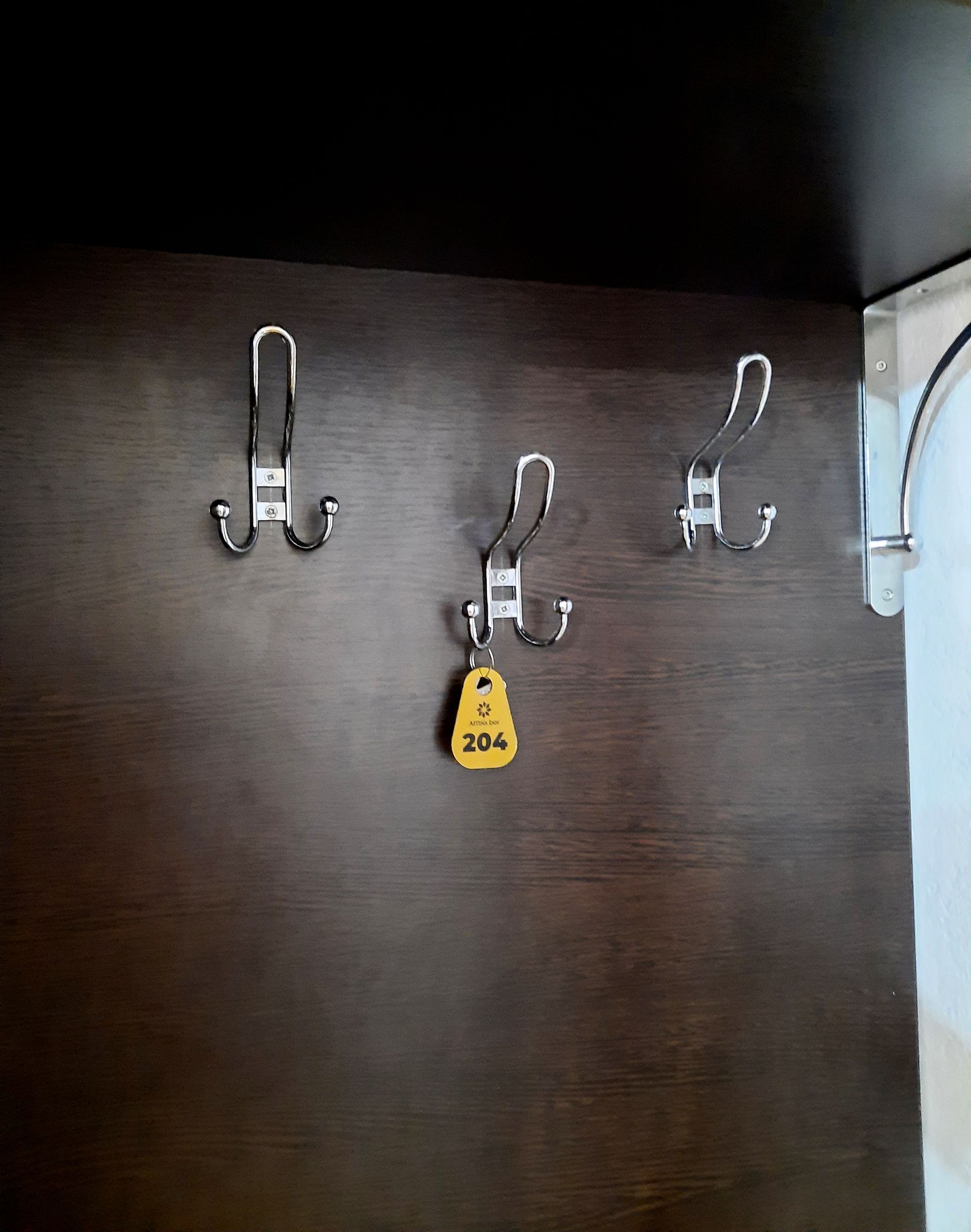 Three metal coat hooks on a dark wooden wall, one with a yellow tag labeled 