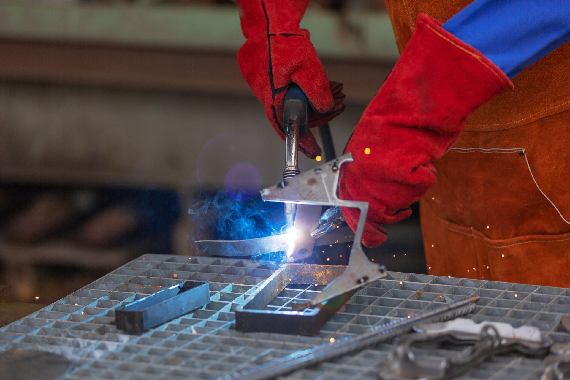 A welder in red gloves welding metal parts on a metal table, sparks flying.