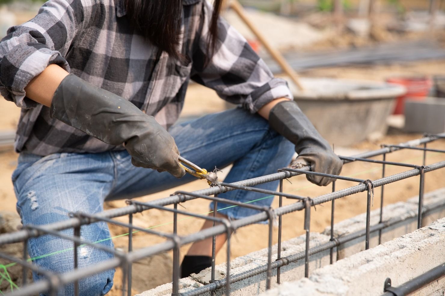 Woman wearing work gloves, tying rebar at a construction site.