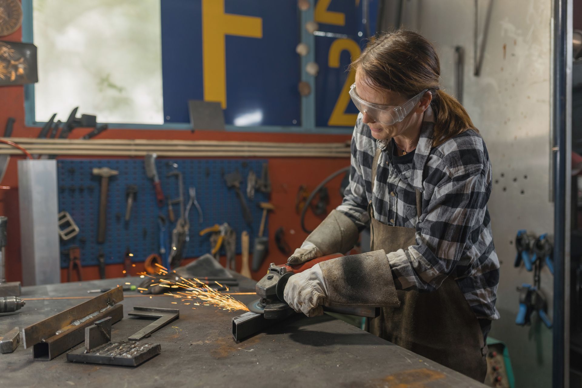 Woman in safety glasses grinding metal in a workshop, sparks flying.