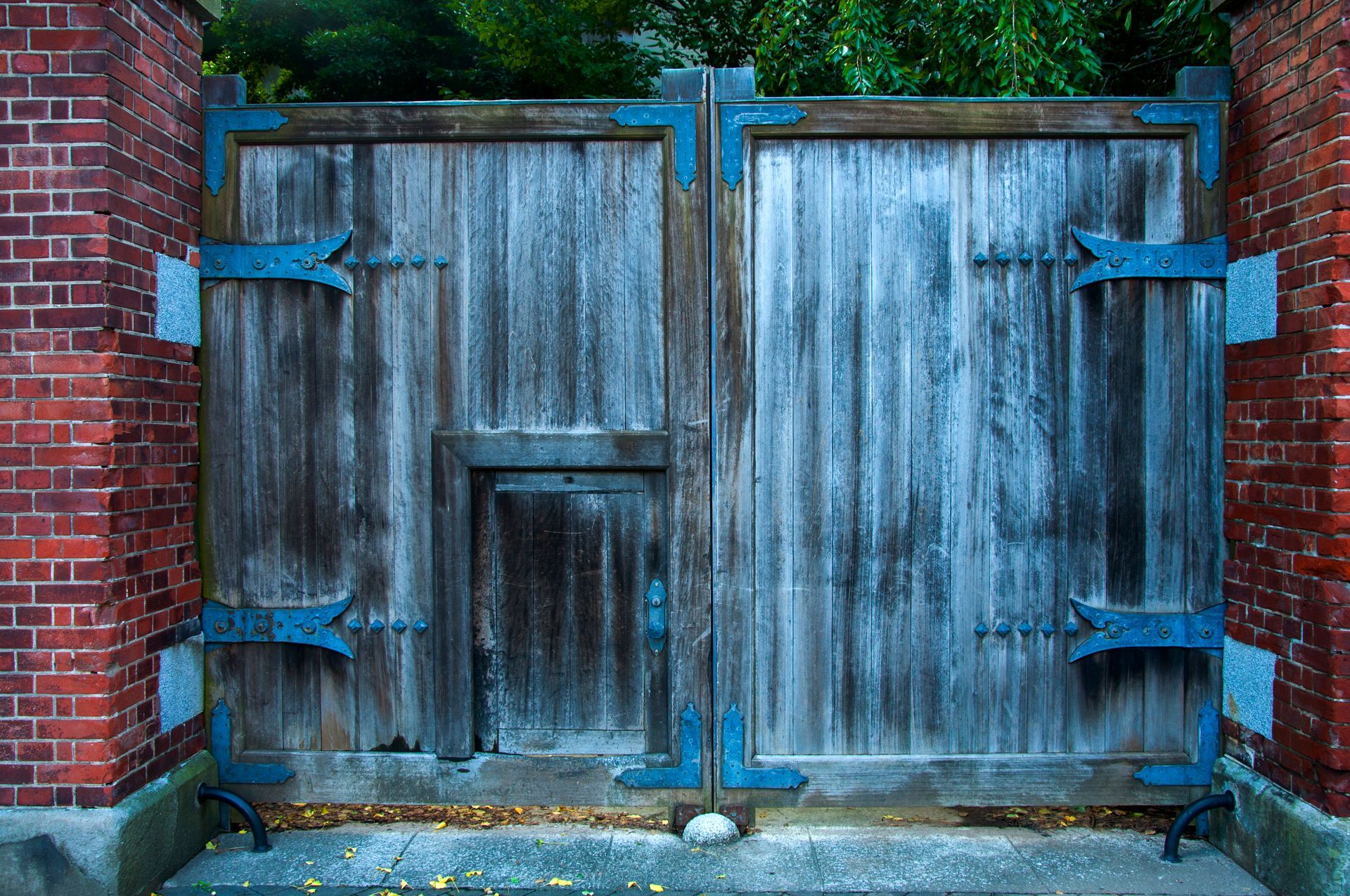 Weathered wooden gate with blue metal hinges, set in brick walls.