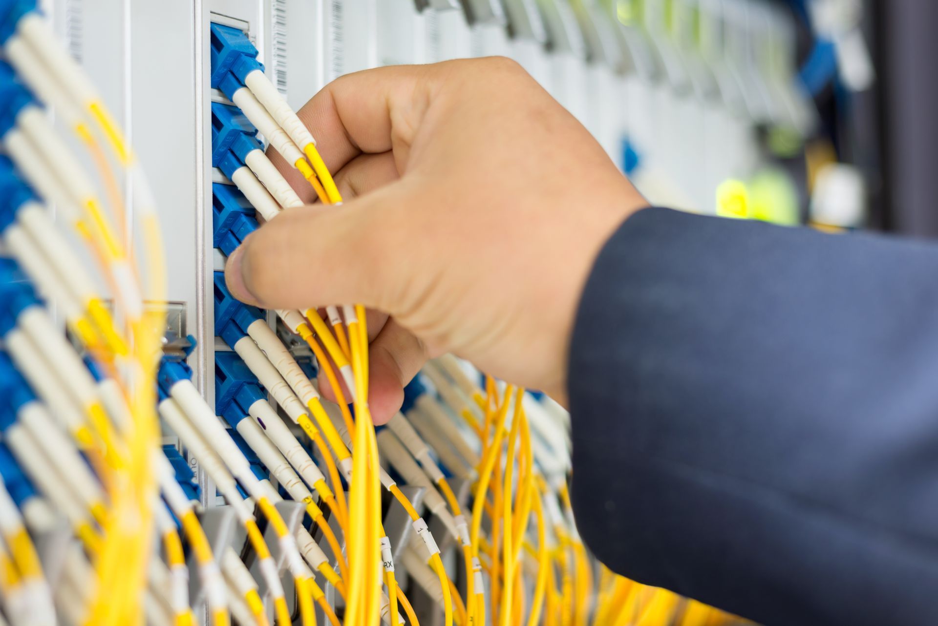 Hand connecting yellow fiber optic cables to a blue server rack.