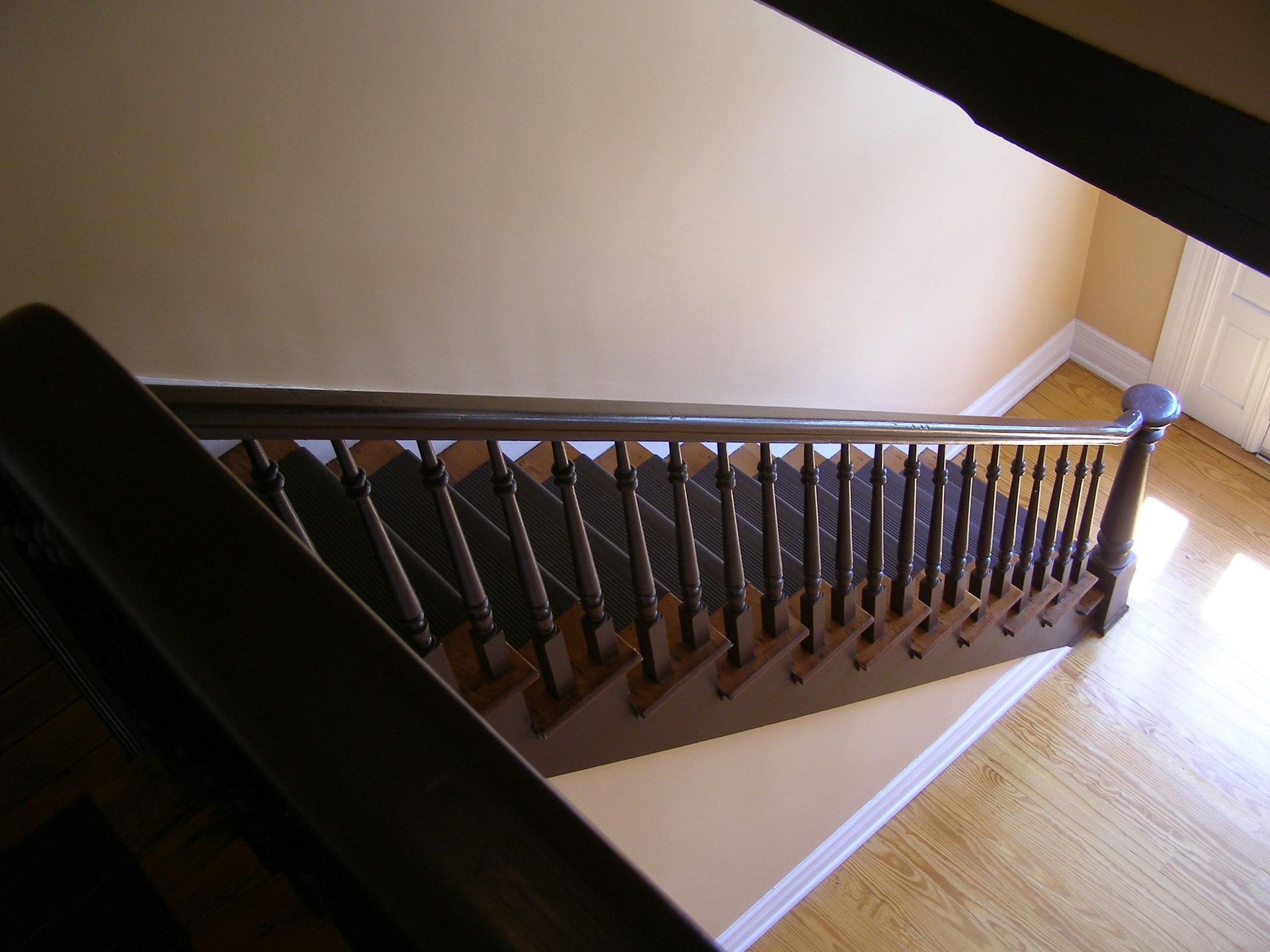 Wooden staircase descending, dark banister, beige walls, hardwood floor.