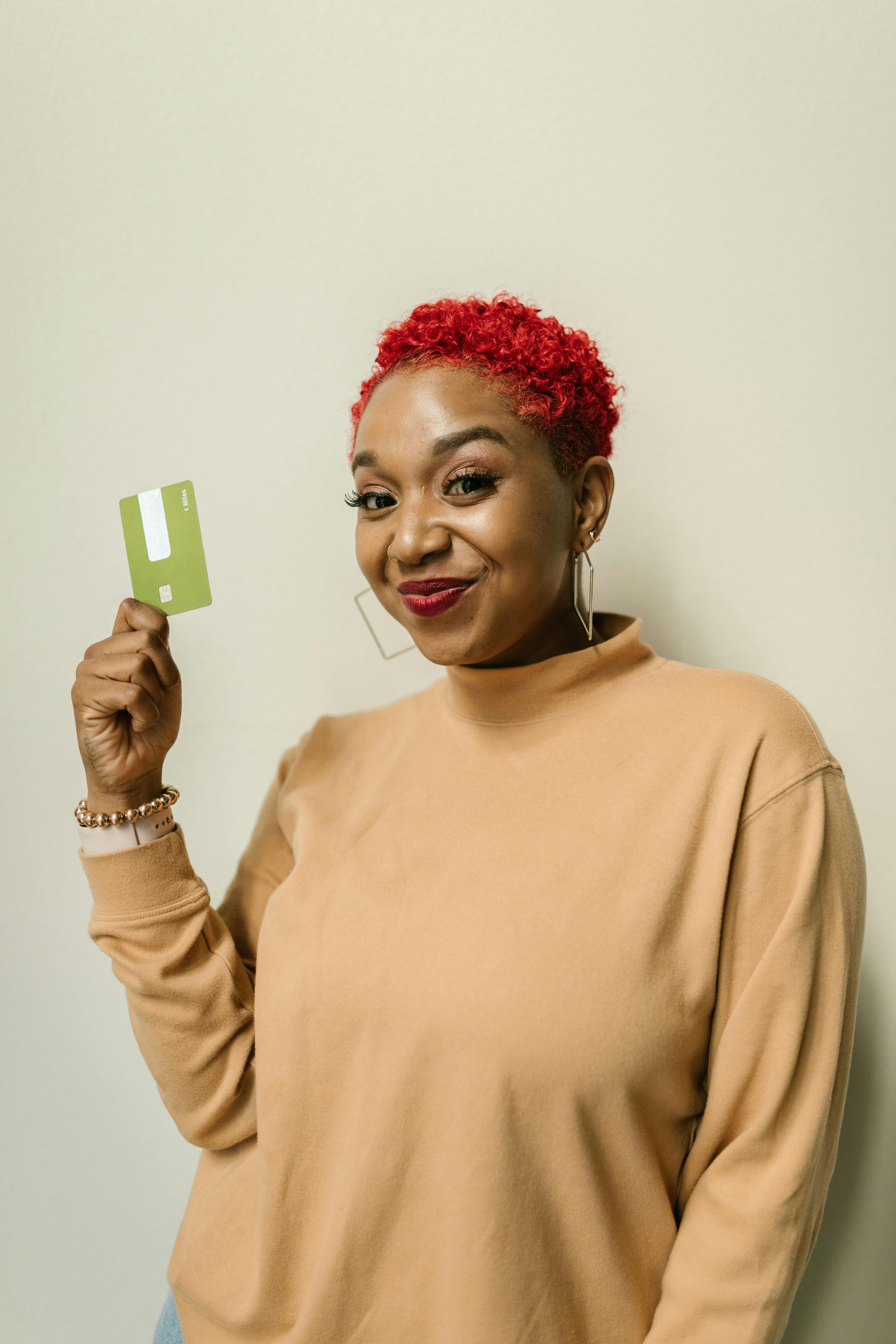 Woman with red hair holding a green card, smiling, wearing an orange sweater.