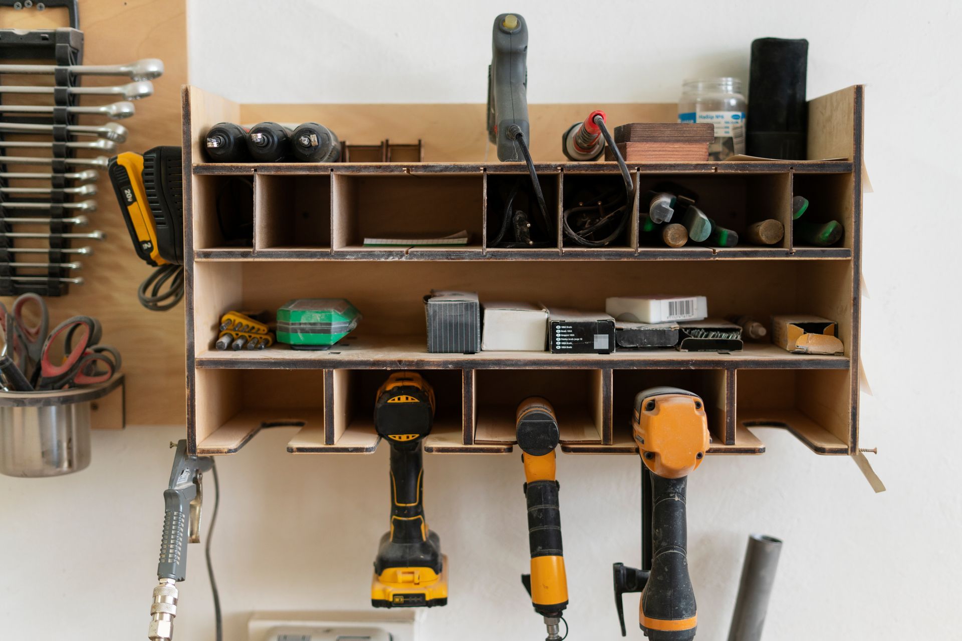 Wooden tool organizer mounted on a white wall, holding tools and small items.