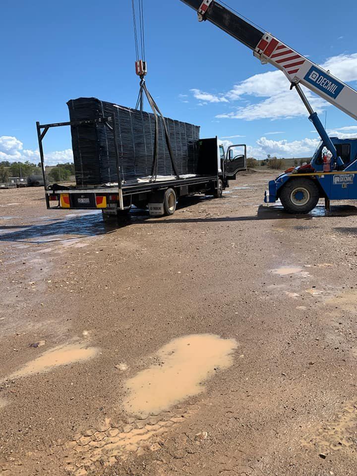 A Crane Lifting a Stack of Black Materials From a Flatbed Truck on a Muddy, Outdoor Lot — Quik As Couriers in Rosella, QLD