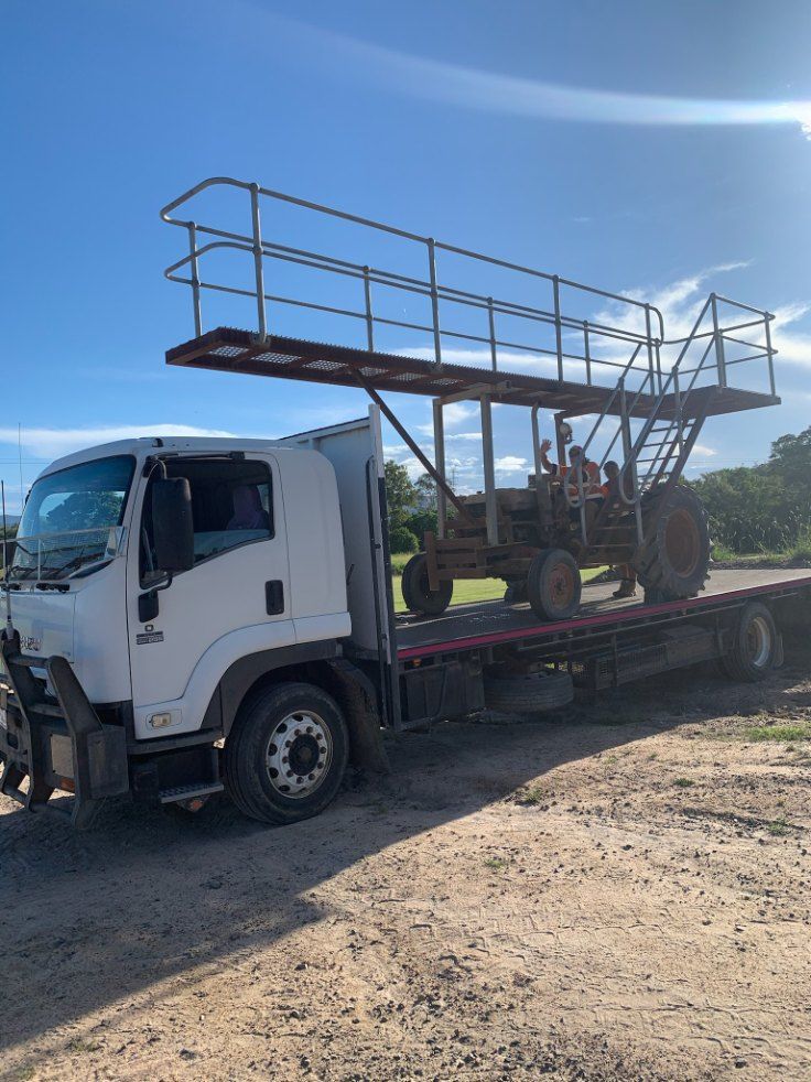 White Truck Carrying a Tractor With an Elevated Platform on a Dirt Road Under a Blue Sky  — Quik As Couriers in Rosella, QLD
