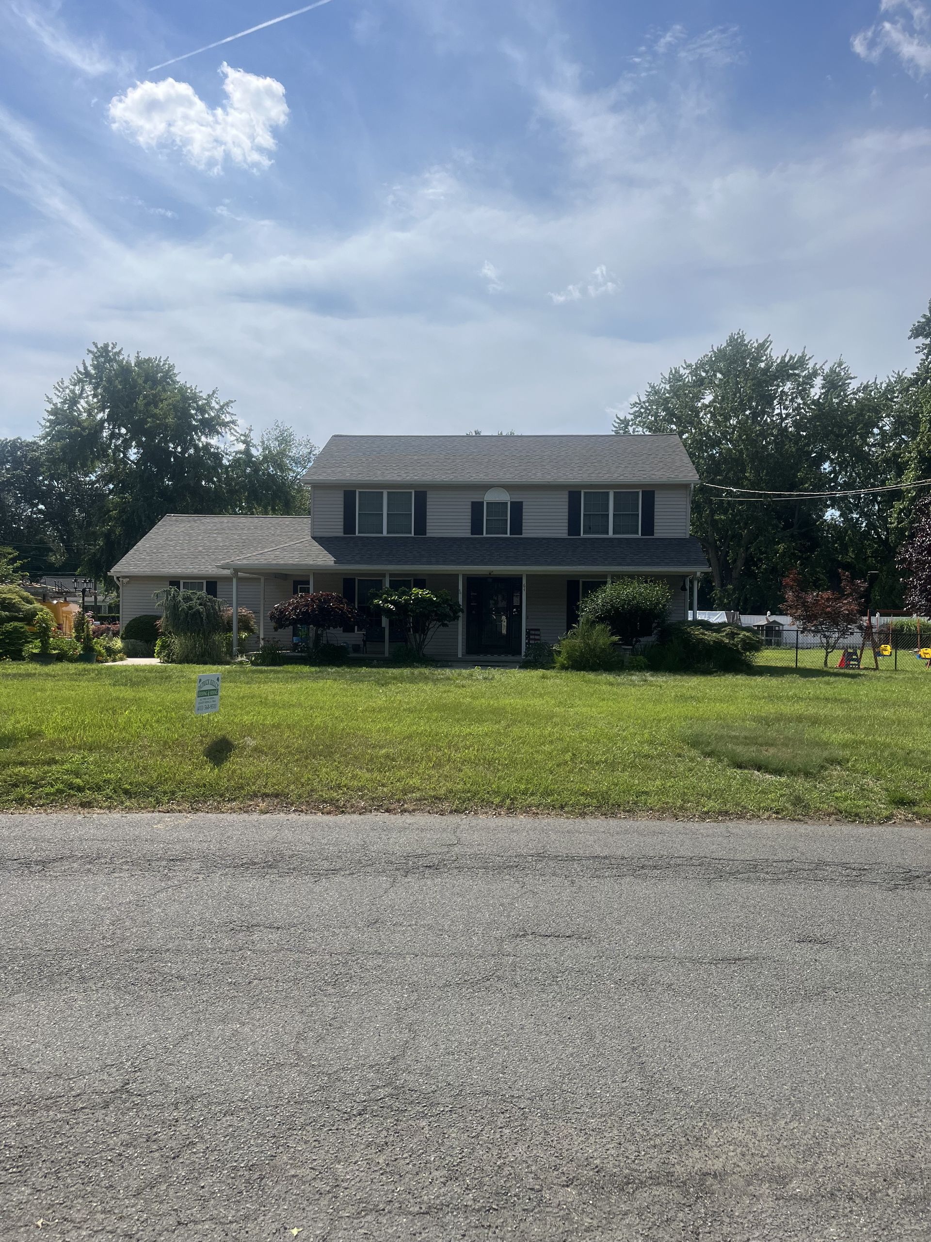 Two-story beige house with a porch, green lawn, and blue sky.