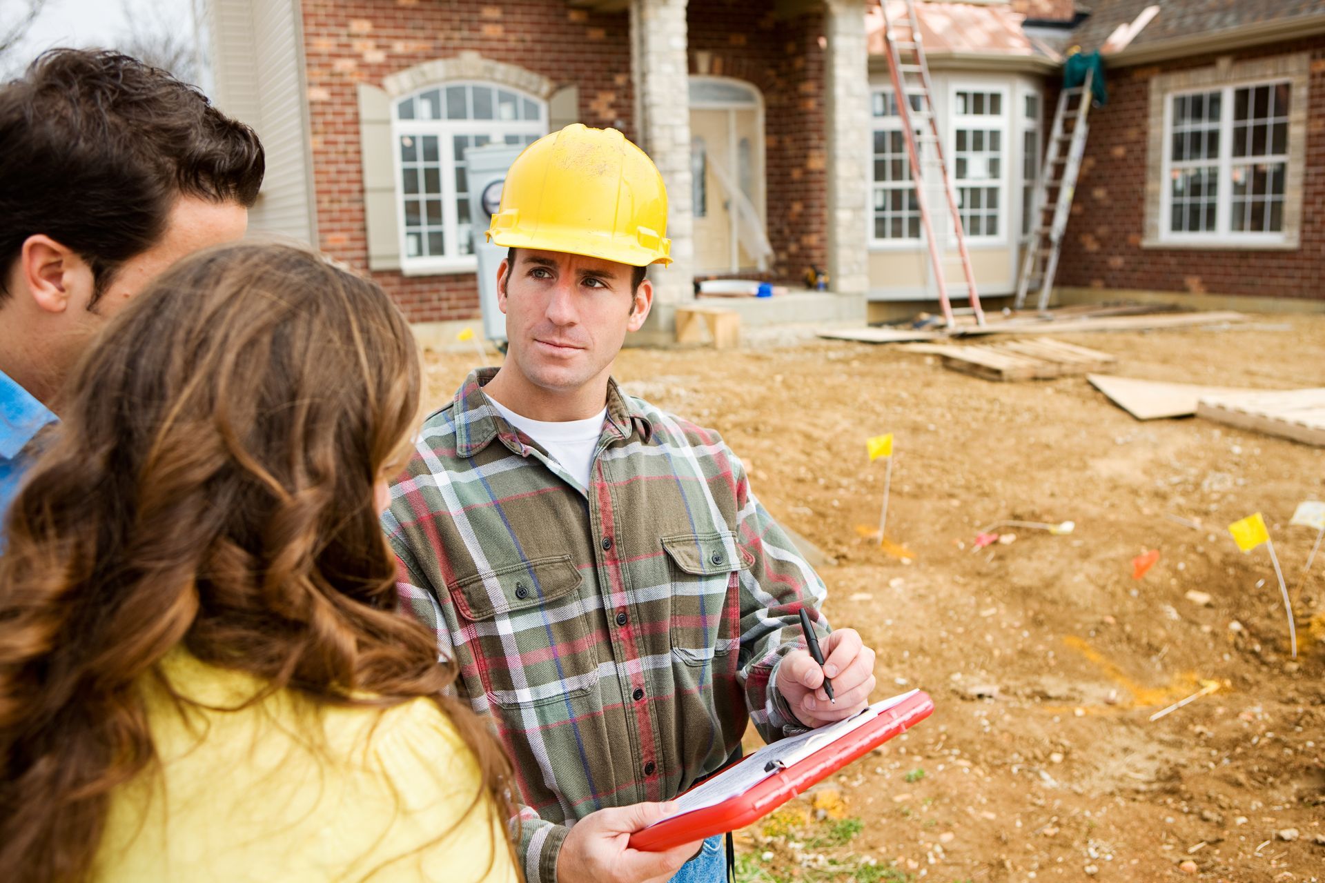 Contractor in hard hat reviewing estimate details with homeowners at a residential exterior project