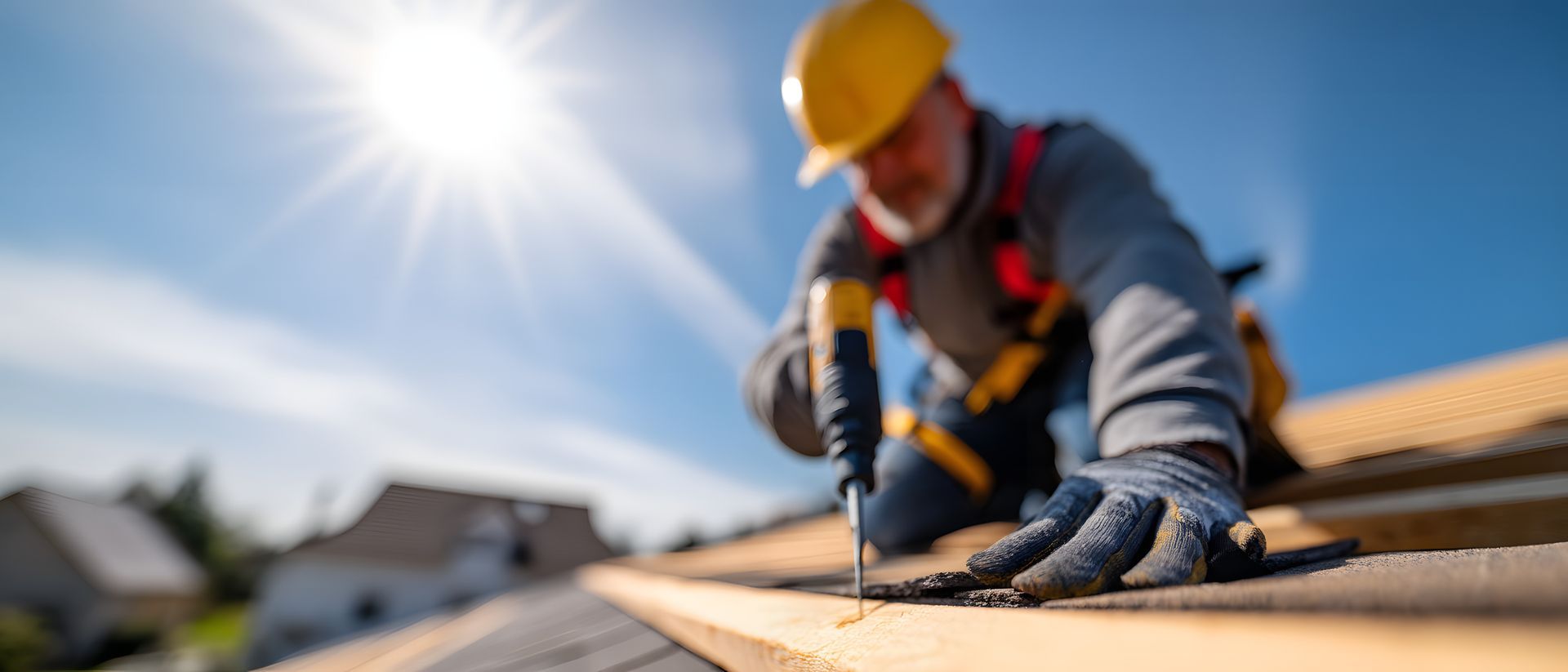 A focused roofer meticulously fastens roofing material under a bright, sunny sky.