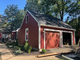 Red-sided garage with dark roof, two garage doors, and a small window; trees in the background.