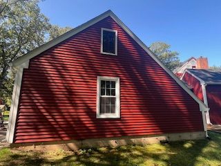 Red wooden building with white-framed windows and a gable roof, set in a yard.