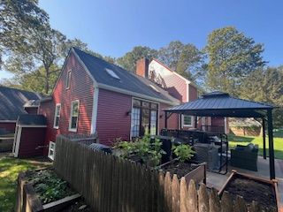 Red house exterior with a black gazebo and garden beds in the yard.
