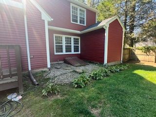 Red house with stone area, small plants, and green lawn.