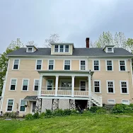 A large house with a large porch is sitting on top of a lush green hillside.
