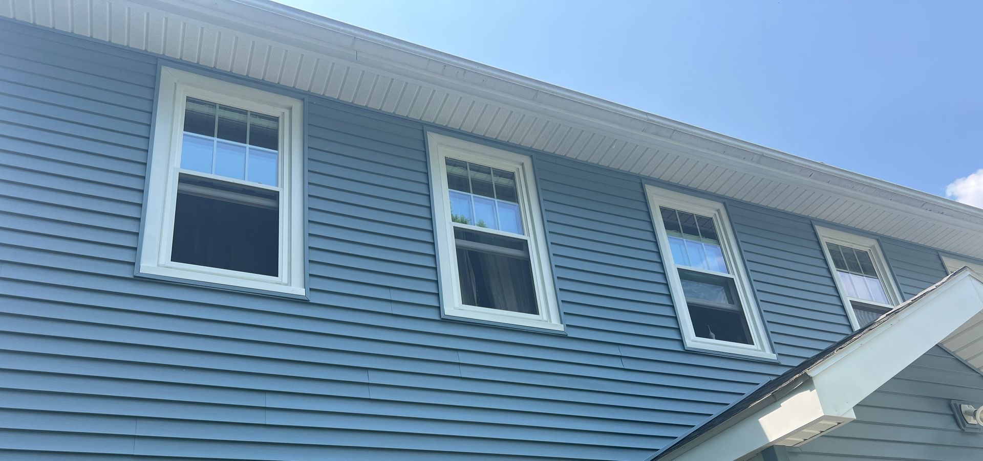 Blue-sided house with white-framed windows under a bright blue sky.