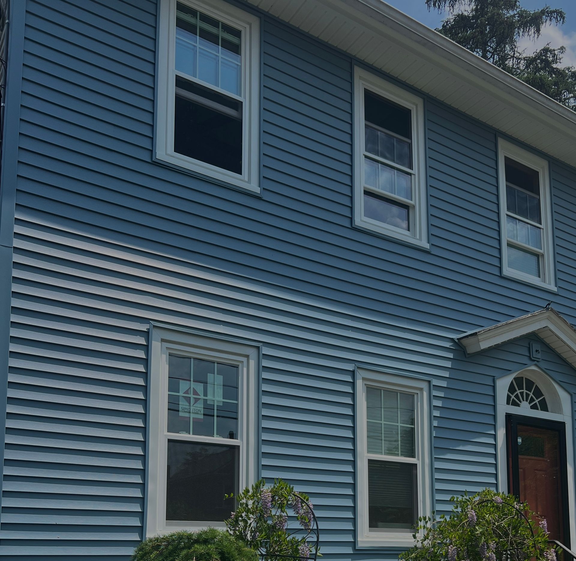 Blue clapboard house with white-framed windows and a brown door.