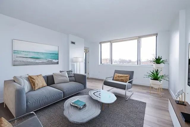 A modern, minimalist living room with a grey sofa, matching armchair, two organic-shaped coffee tables, and a sea painting.