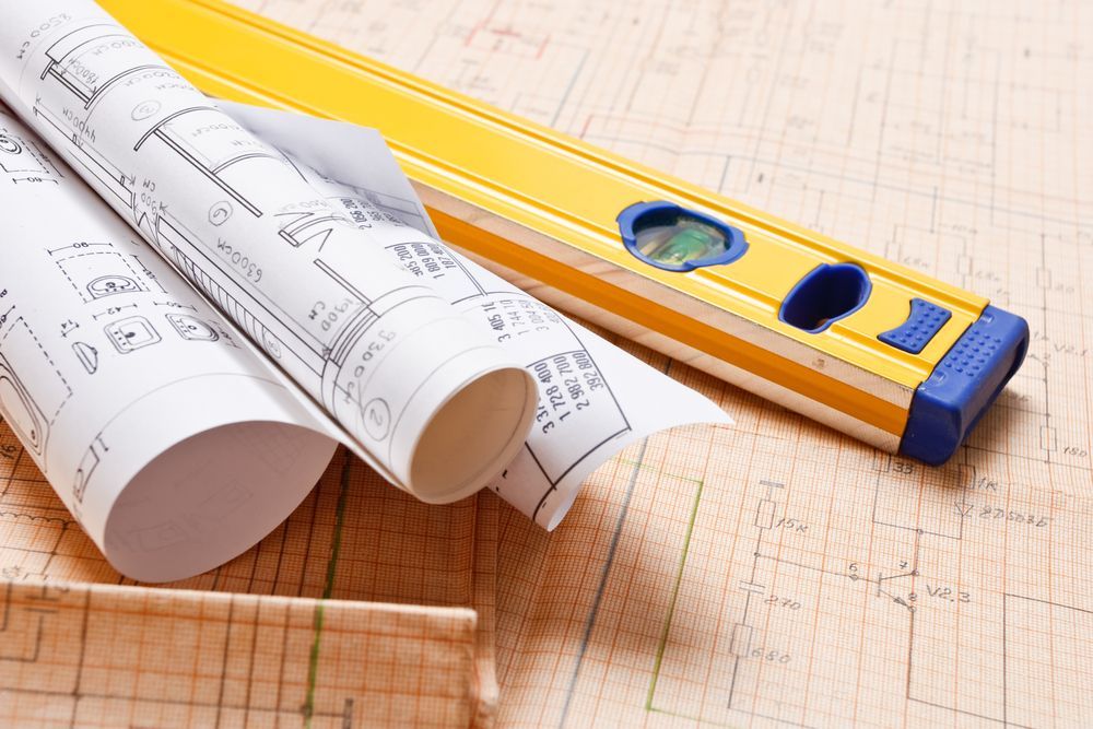 Rolled Blueprints And A Yellow Level On A Grid-lined Surface — GS Design & Drafting In Rous, NSW