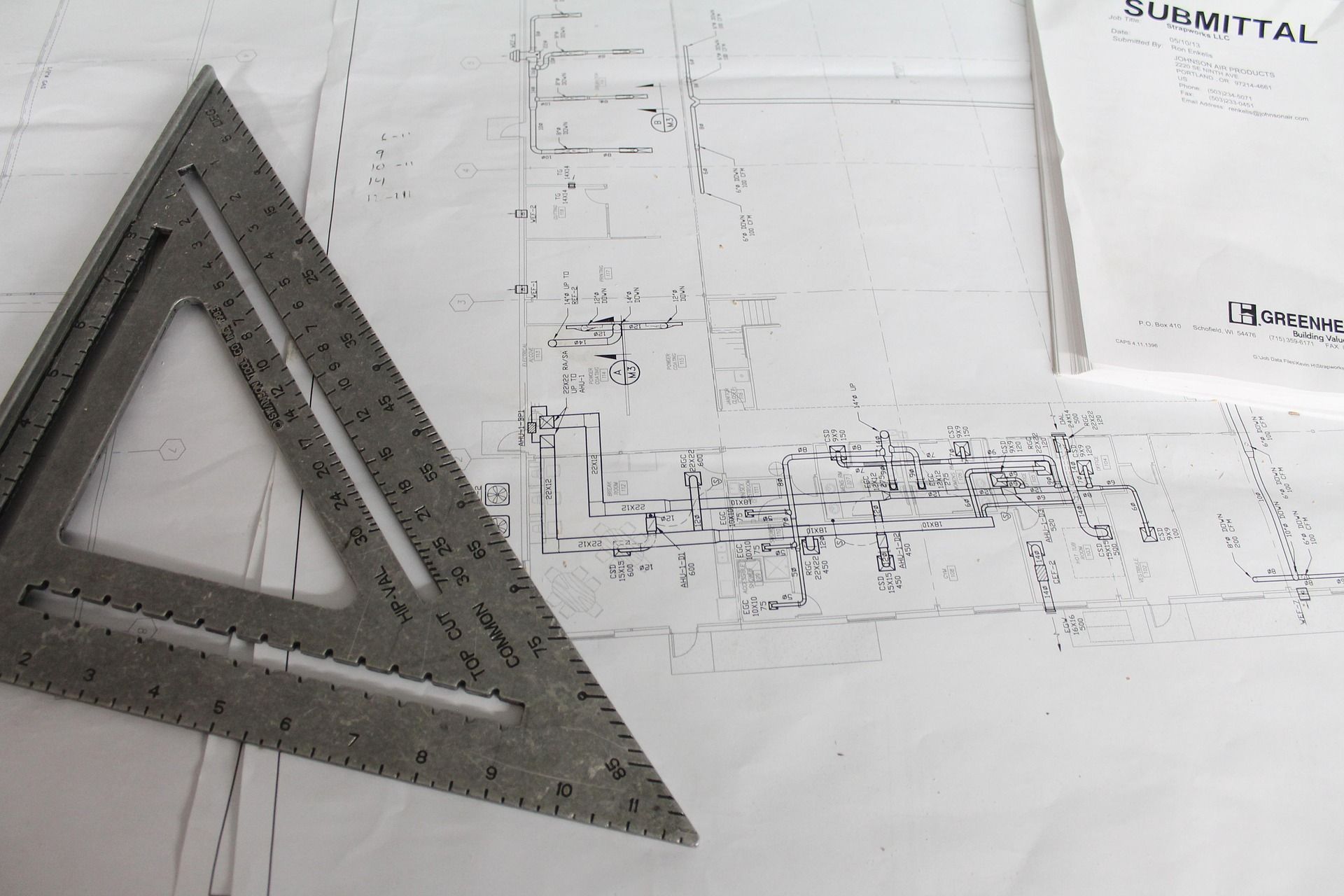 A metal speed square rests on technical blueprints next to a document — GS Design & Drafting In Rous, NSW
