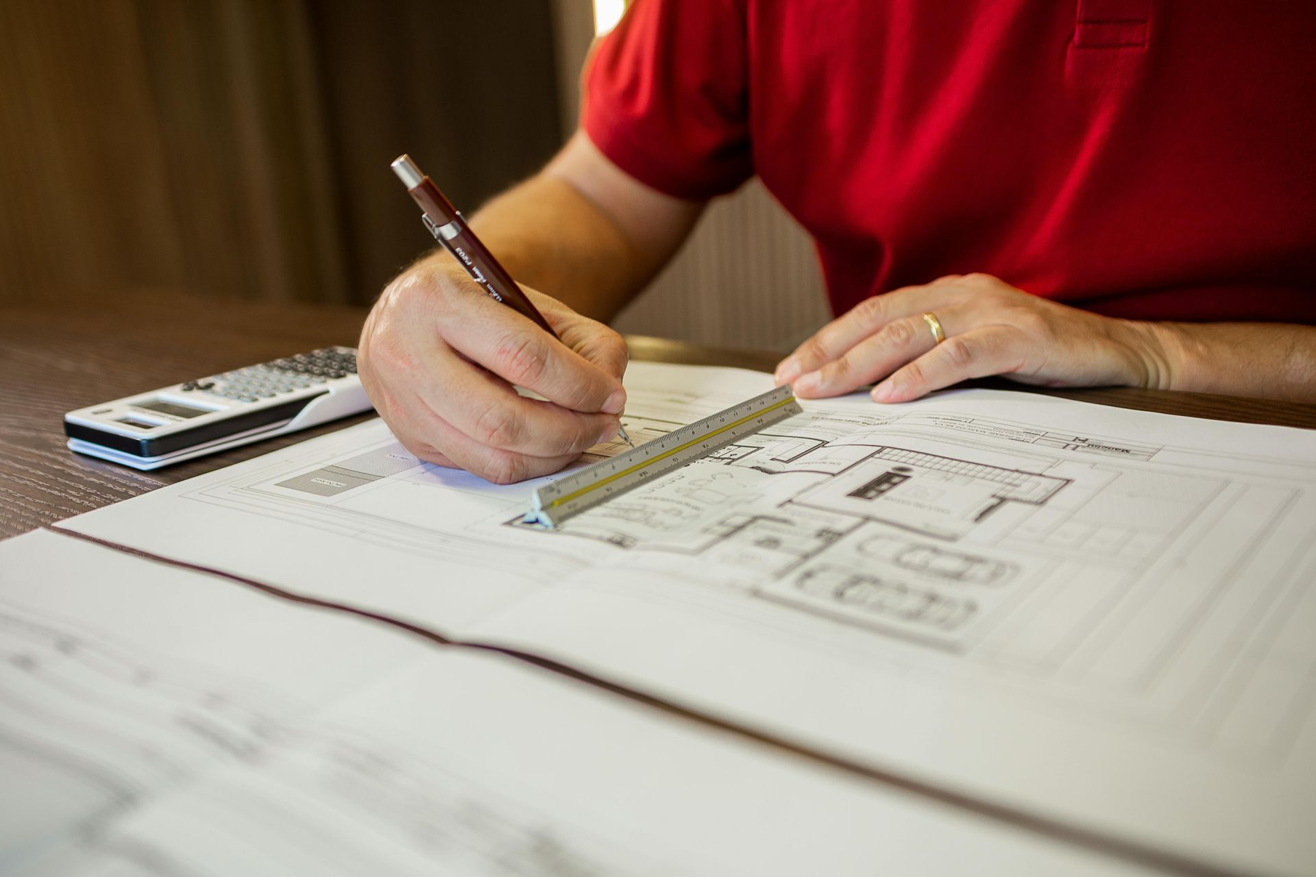 Person In Red Shirt Drawing On Blueprints With A Ruler And Pencil — GS Design & Drafting In Lismore, NSW