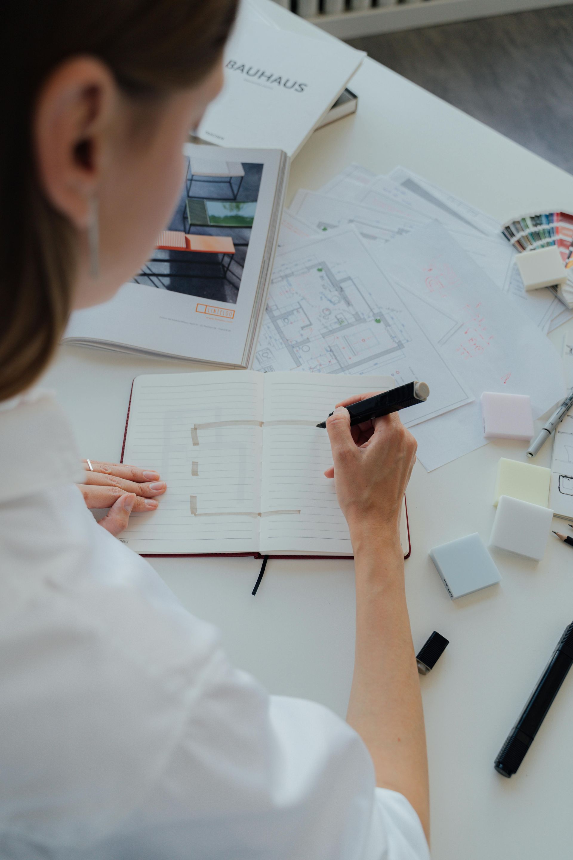Person Sketching On A Notebook At A White Desk With Architectural Plans — GS Design & Drafting In Rous, NSW
