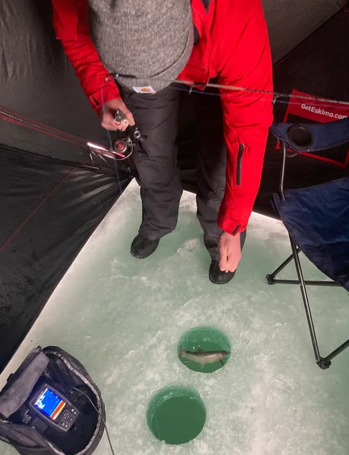 A man in a red jacket is fishing in a tent.