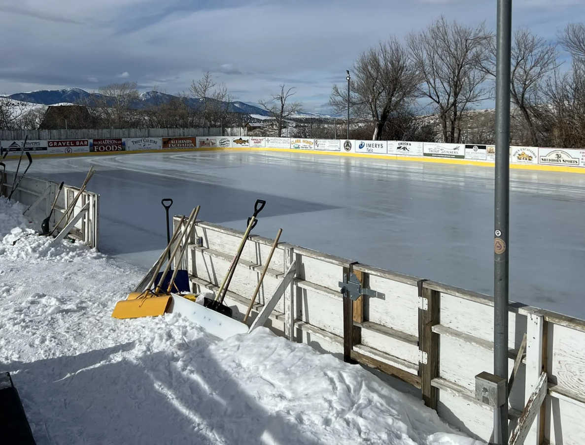 A fence surrounding an ice rink with snow shovels on it.