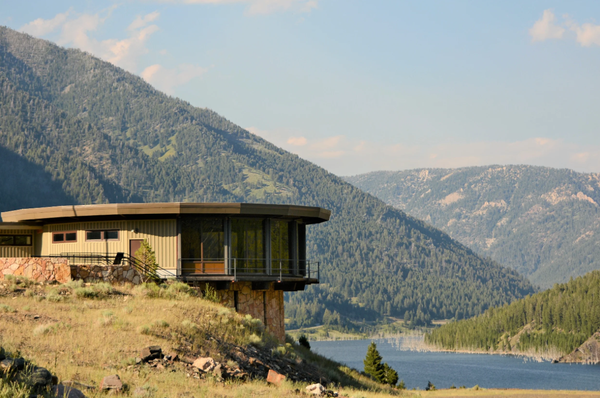 A house on a hill overlooking a lake with mountains in the background.