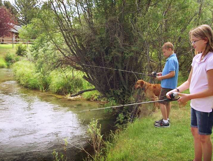 A boy and a girl are fishing in a river with their dog.
