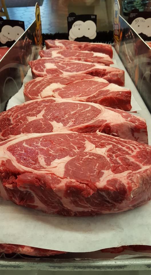 A row of raw steaks sitting on top of each other on a tray.