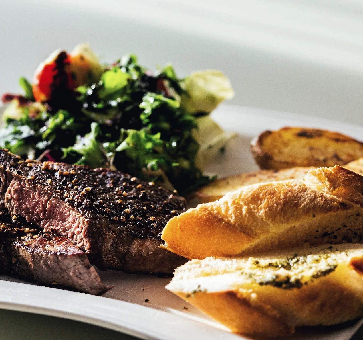 A white plate topped with a steak salad and bread