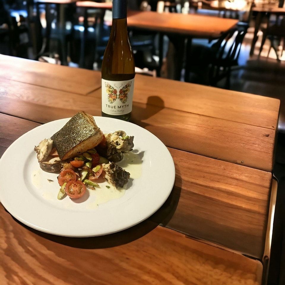 A plate of food is sitting on a wooden table next to a bottle of wine.