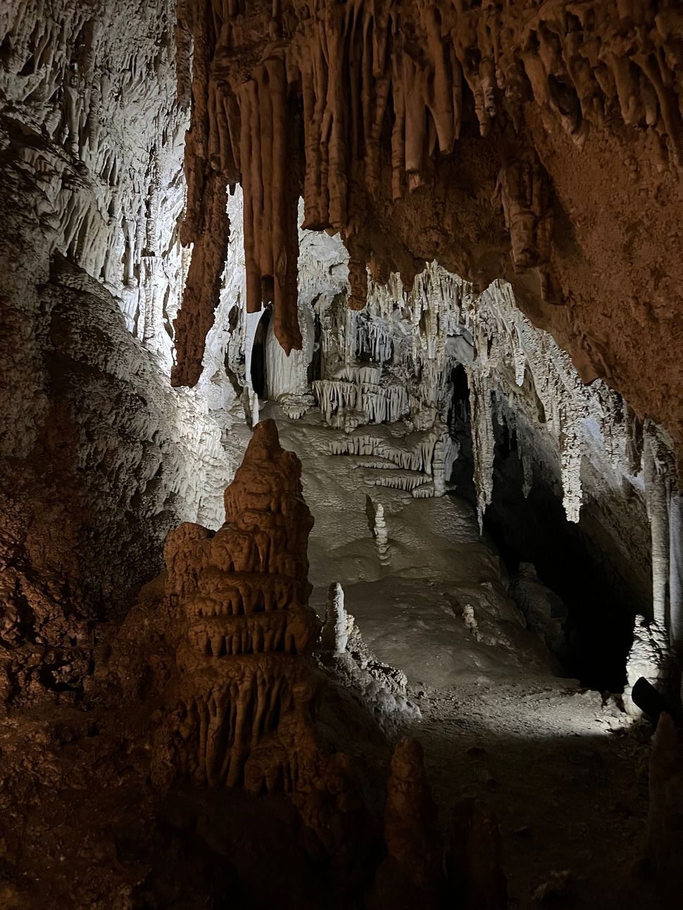 A cave with a lot of rock formations and a light shining through the ceiling.