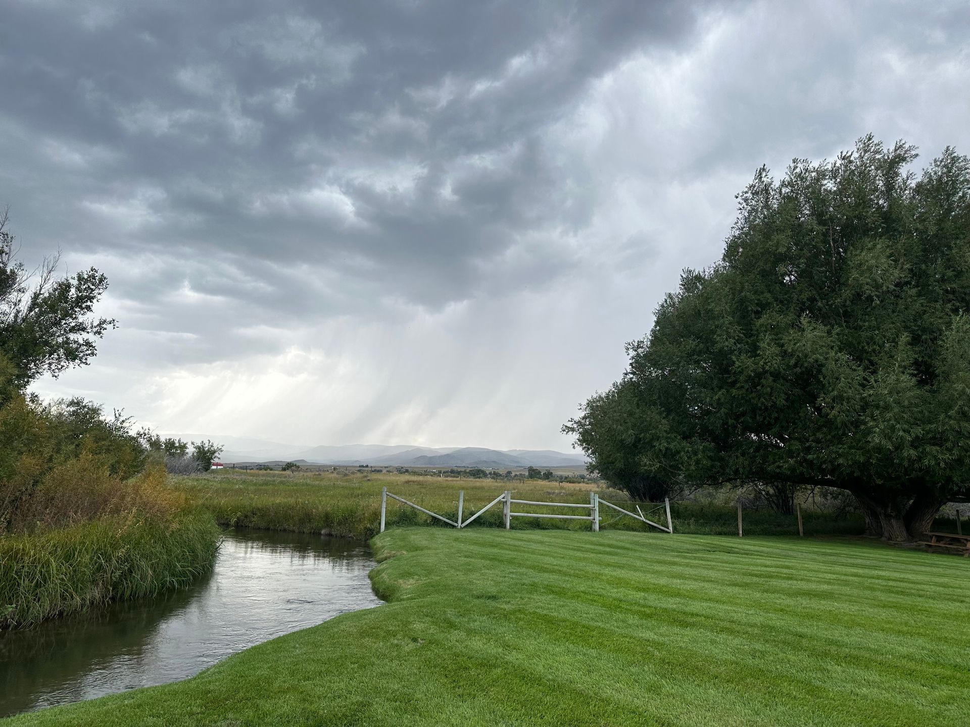 A river running through a lush green field with a white fence in the foreground.