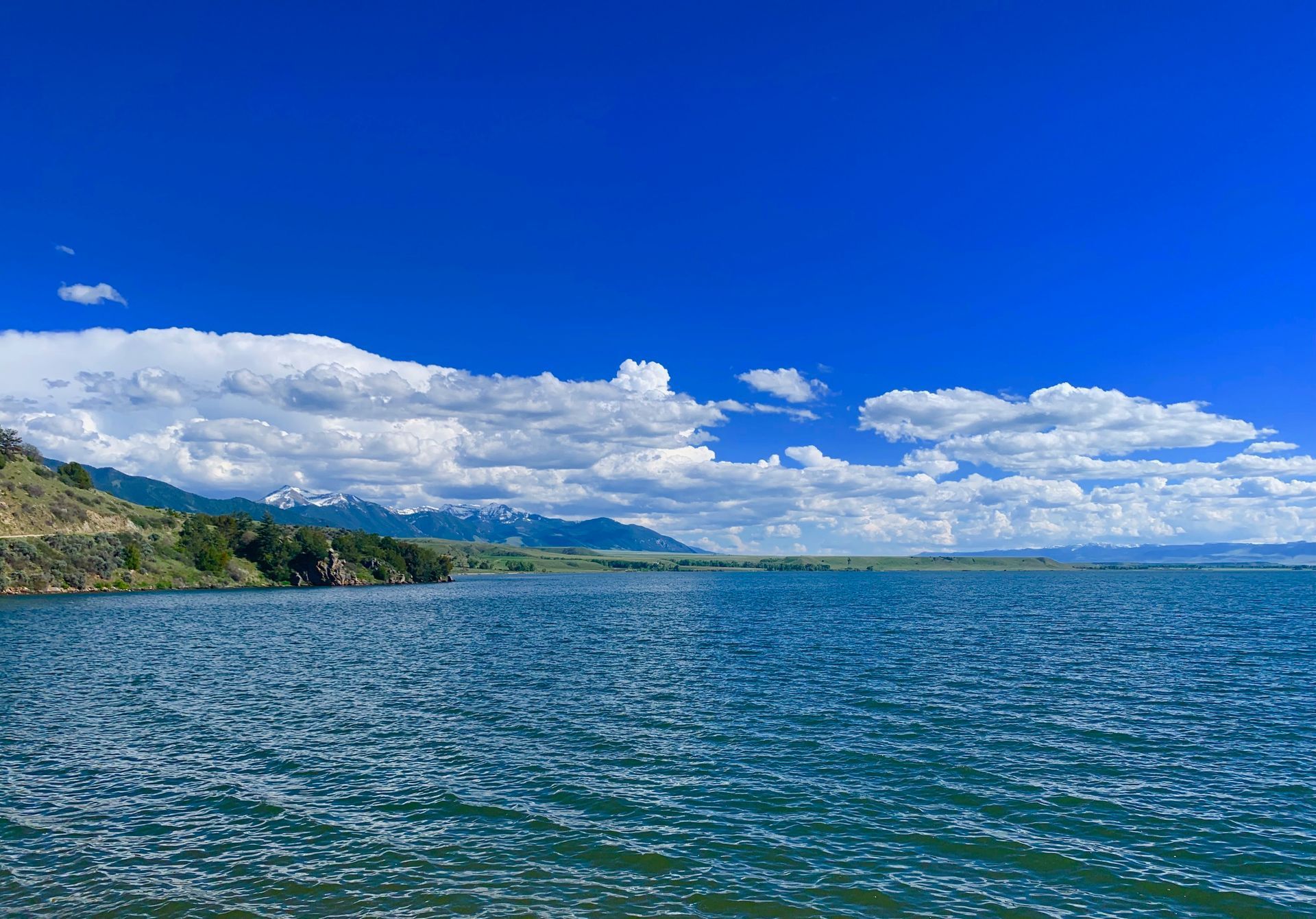 A large body of water with mountains in the background and a blue sky with clouds.