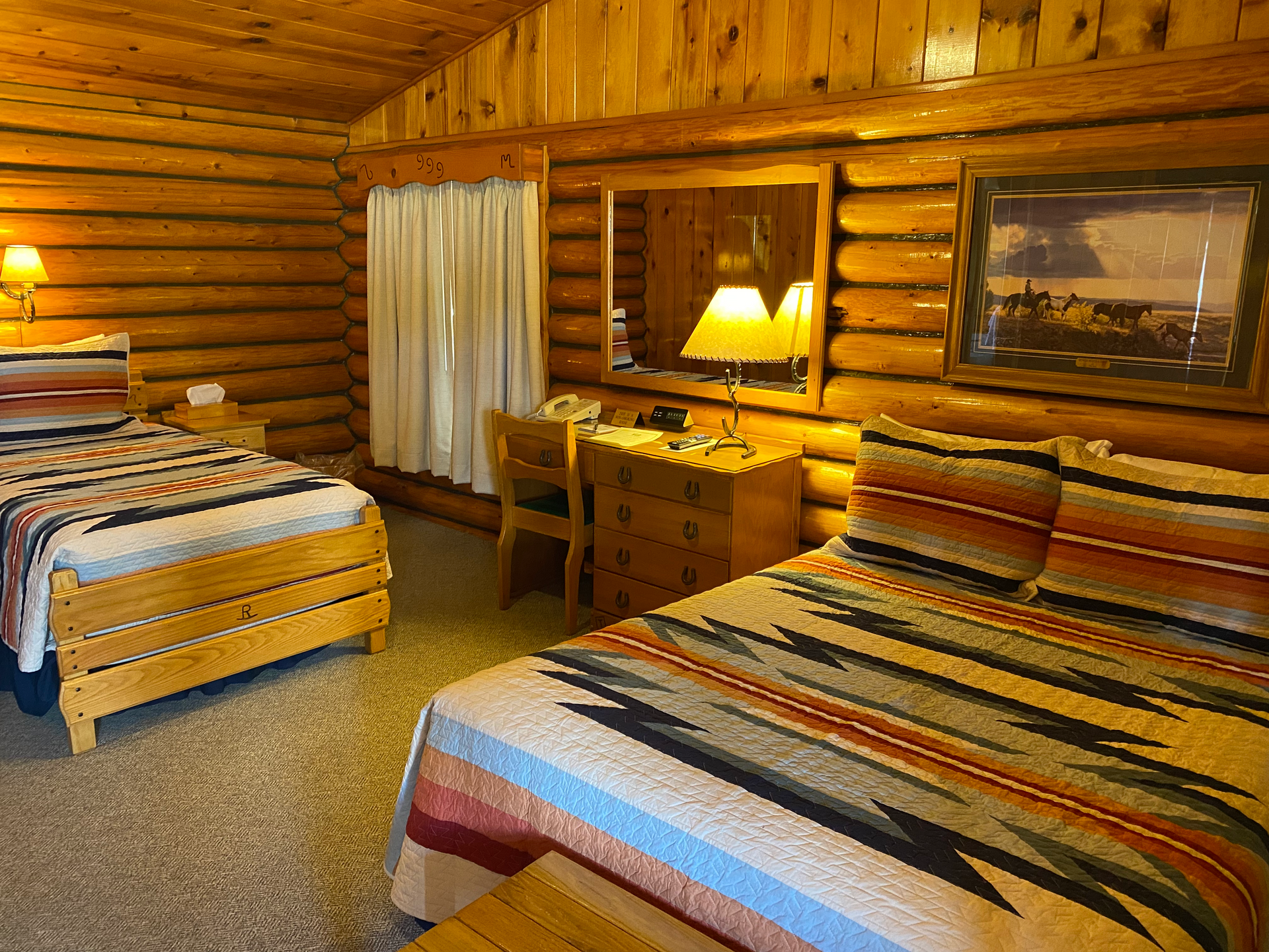 A bedroom in a log cabin with two beds and a desk.