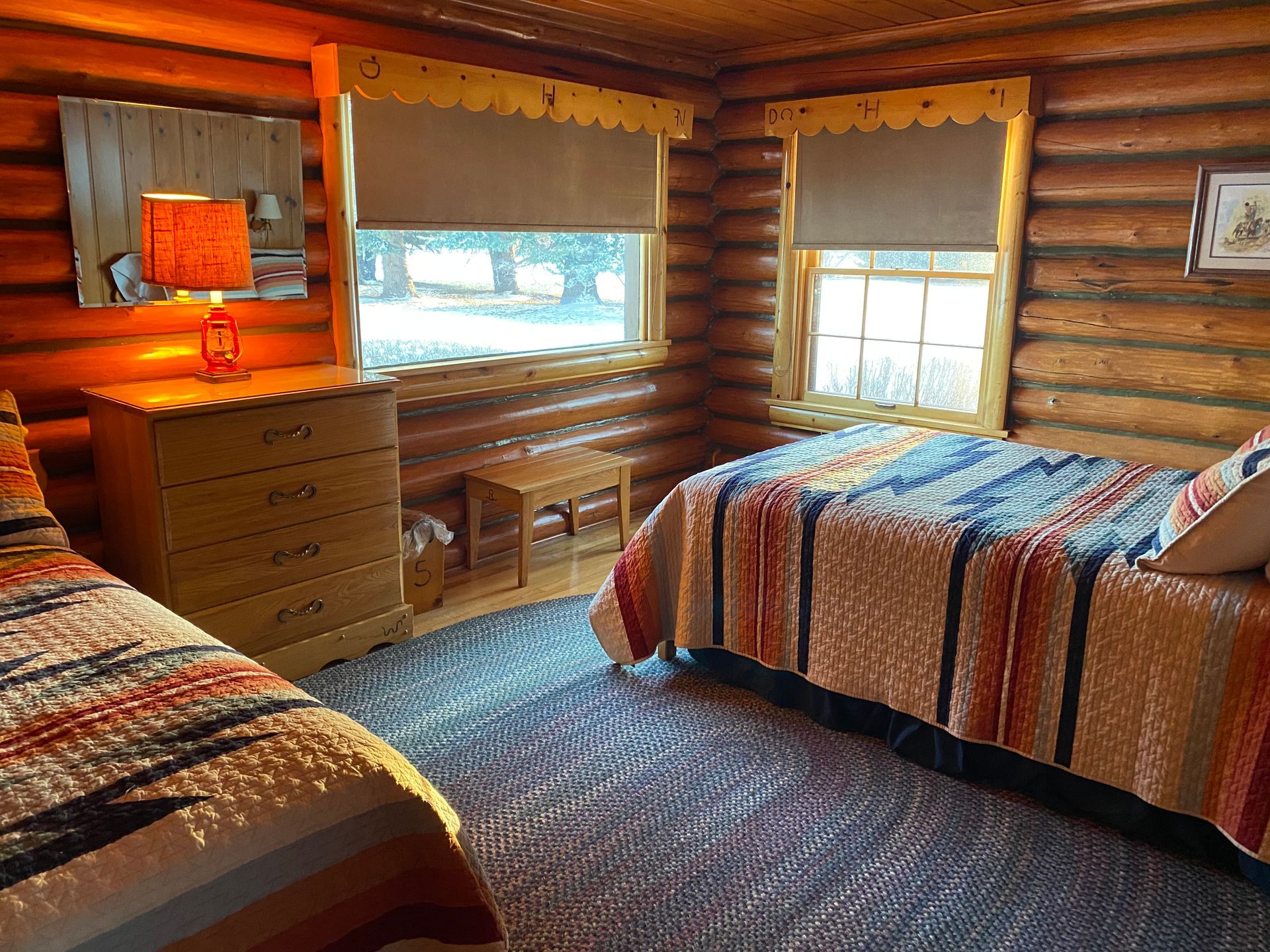 A bedroom in a log cabin with two beds and a dresser.