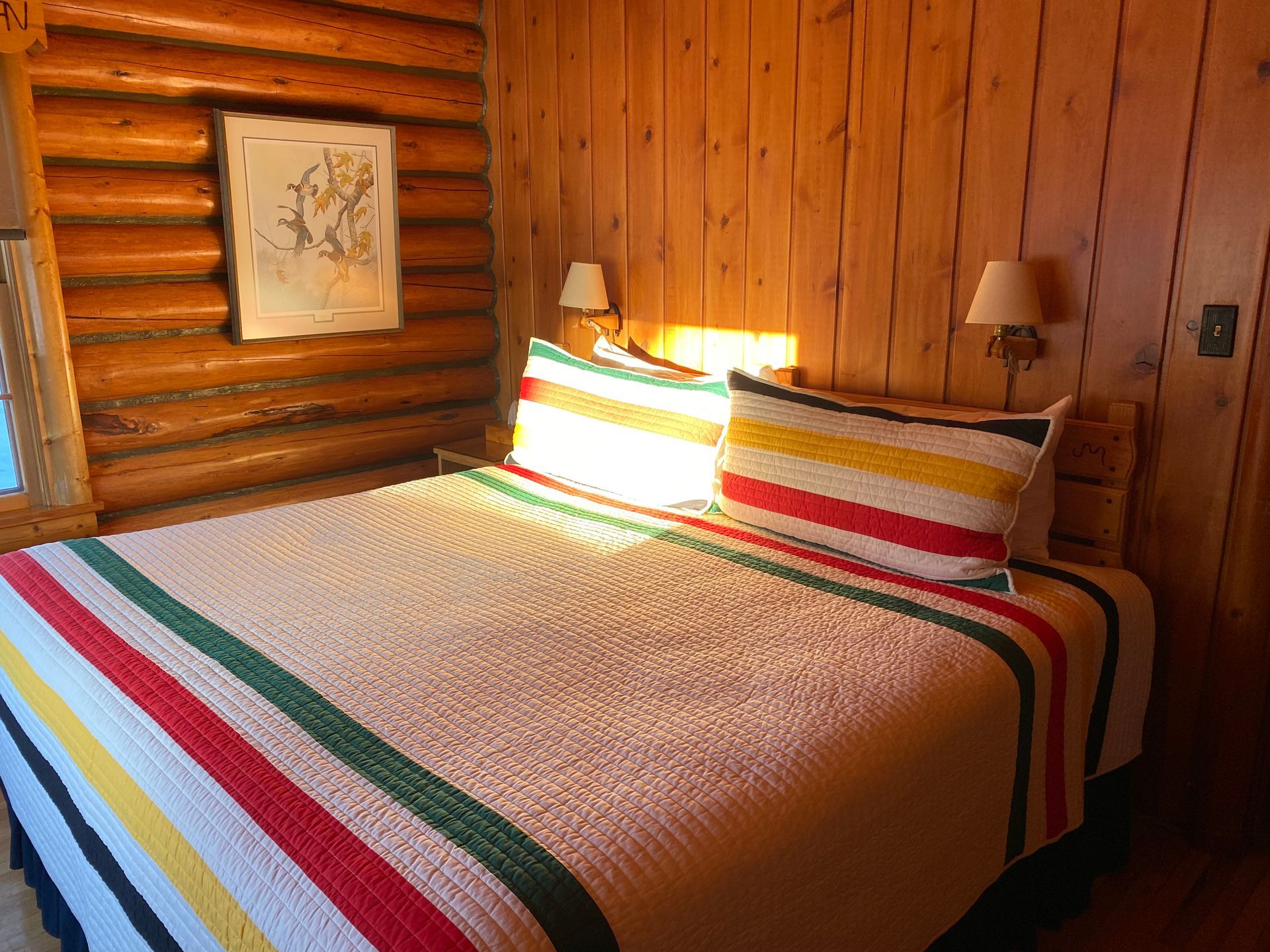 A bed with a striped blanket and pillows in a log cabin.