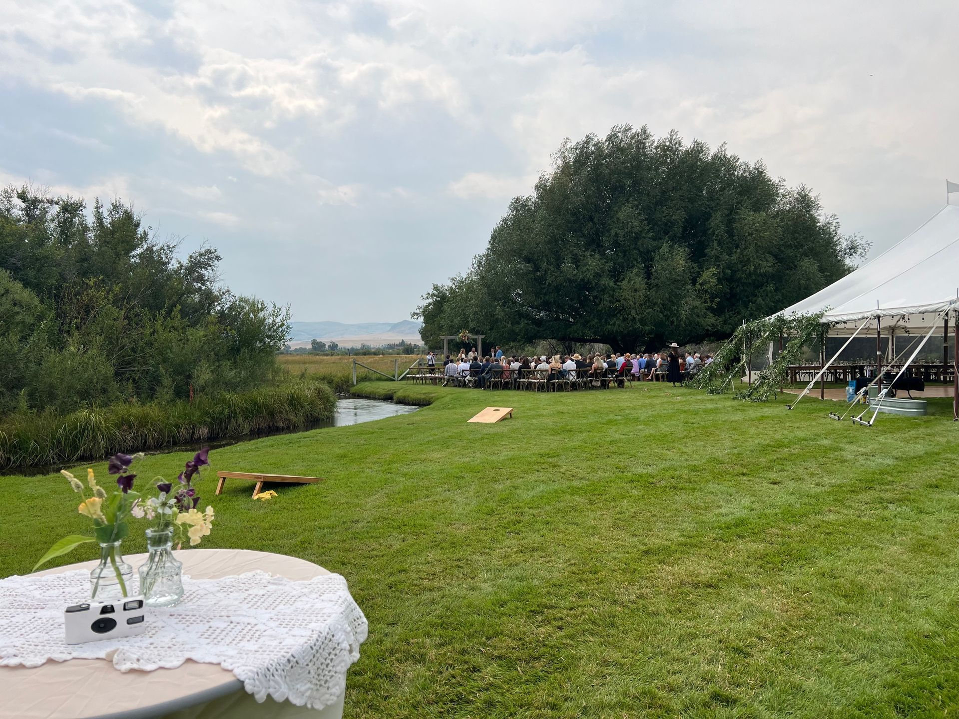 Beautiful meadow with wedding ceremony next to a meandering creek, with event tent and activities for guests.