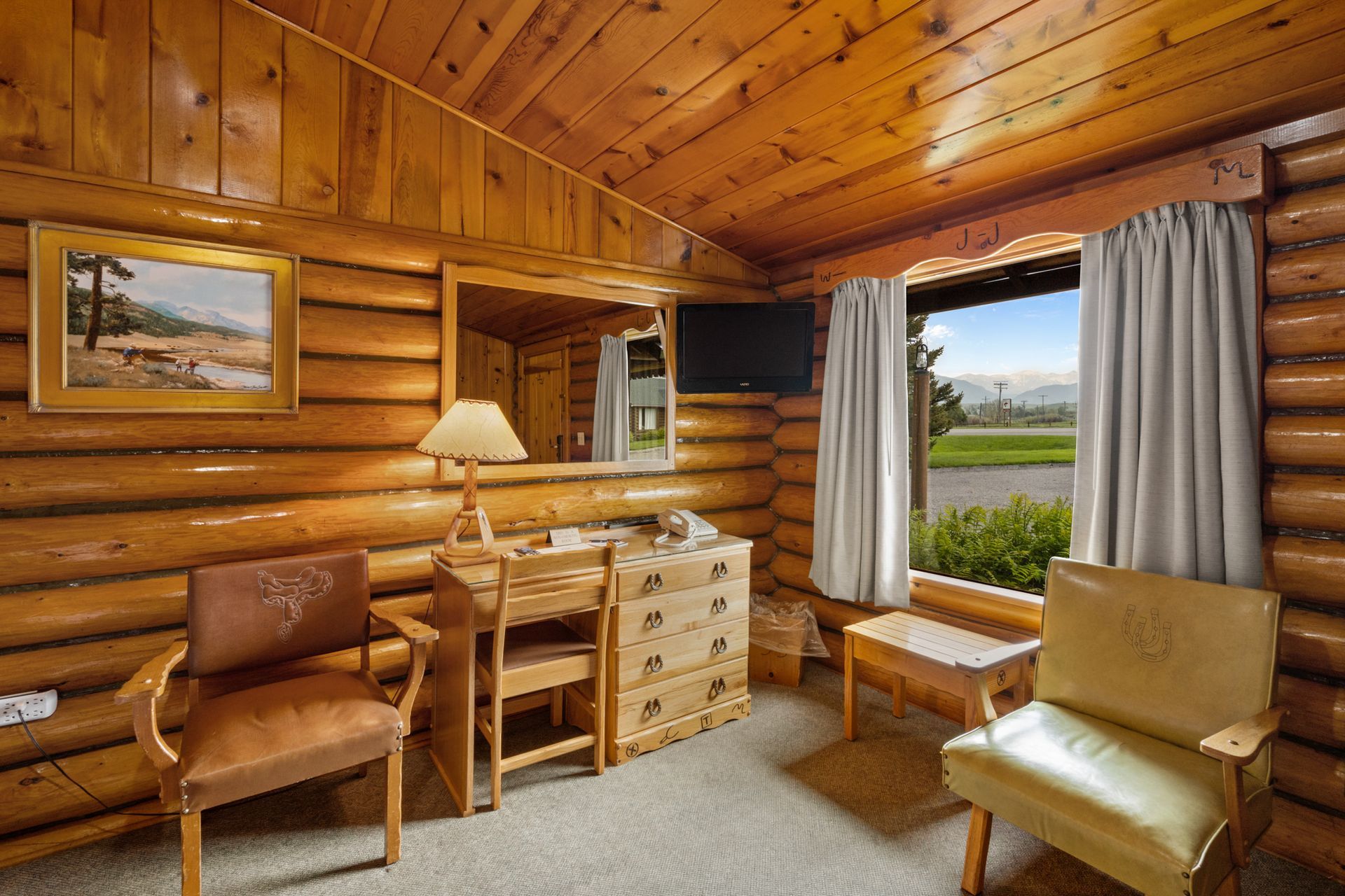 A log cabin with a desk , chairs , dresser and television.