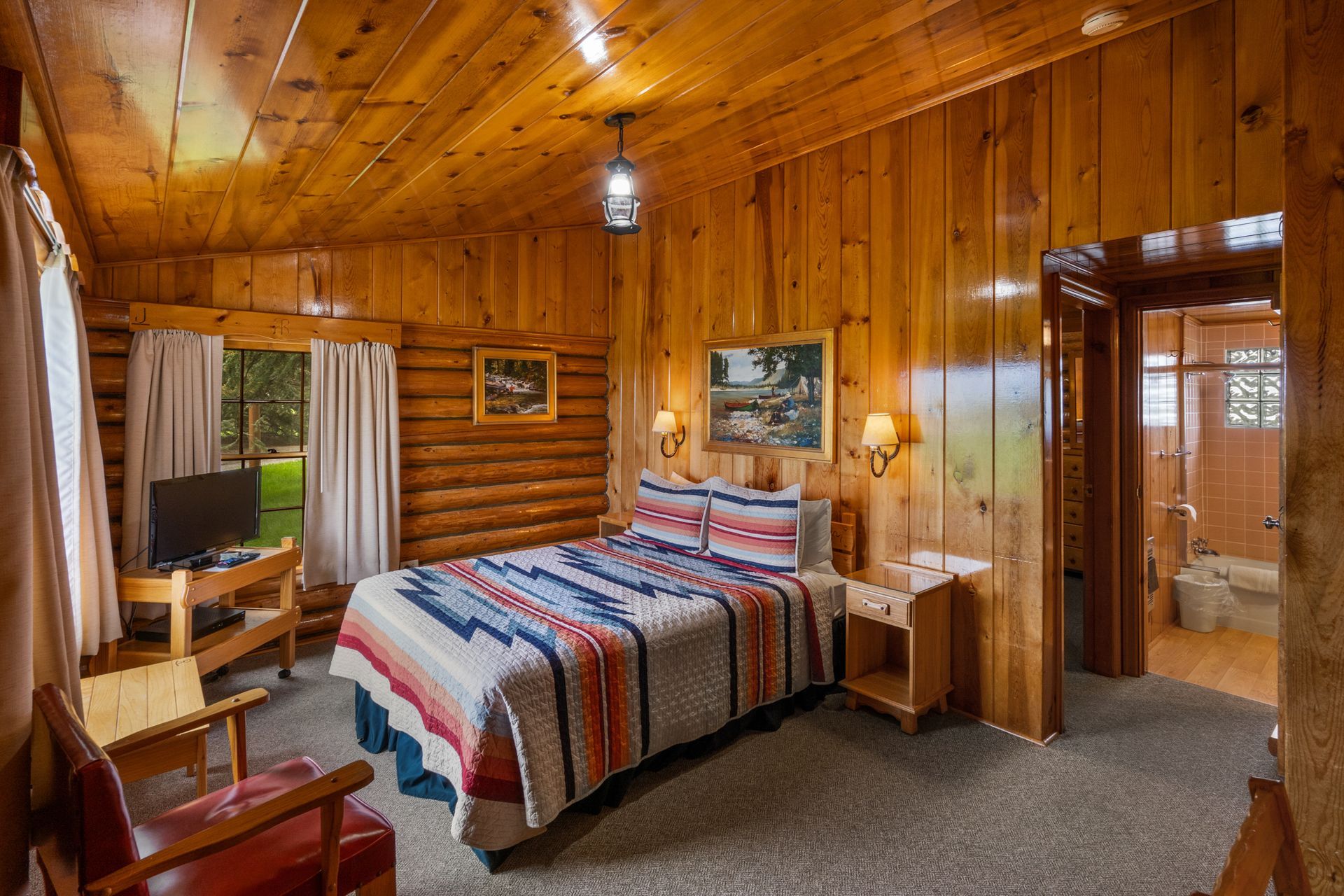 A bedroom in a log cabin with a bed , chair and television.