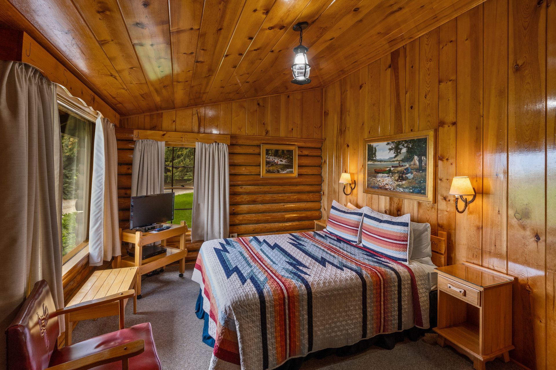 A bedroom in a log cabin with a bed , chair , nightstand and television.