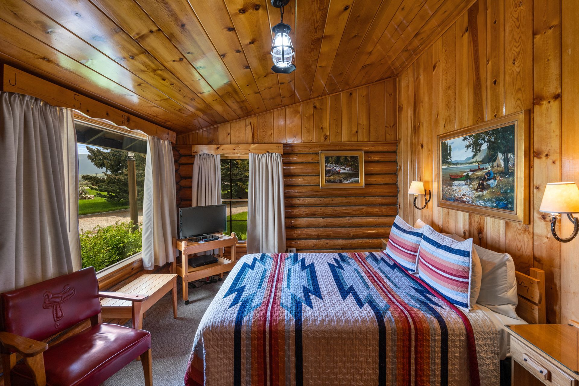A bedroom in a log cabin with a bed , chair , table and television.