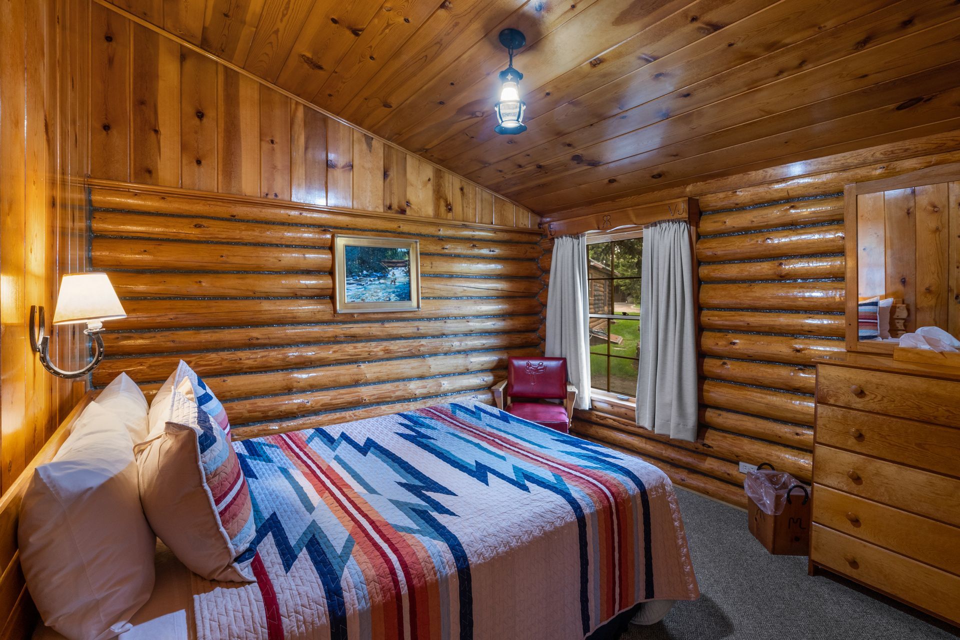 A bedroom in a log cabin with a bed , dresser , chair and mirror.
