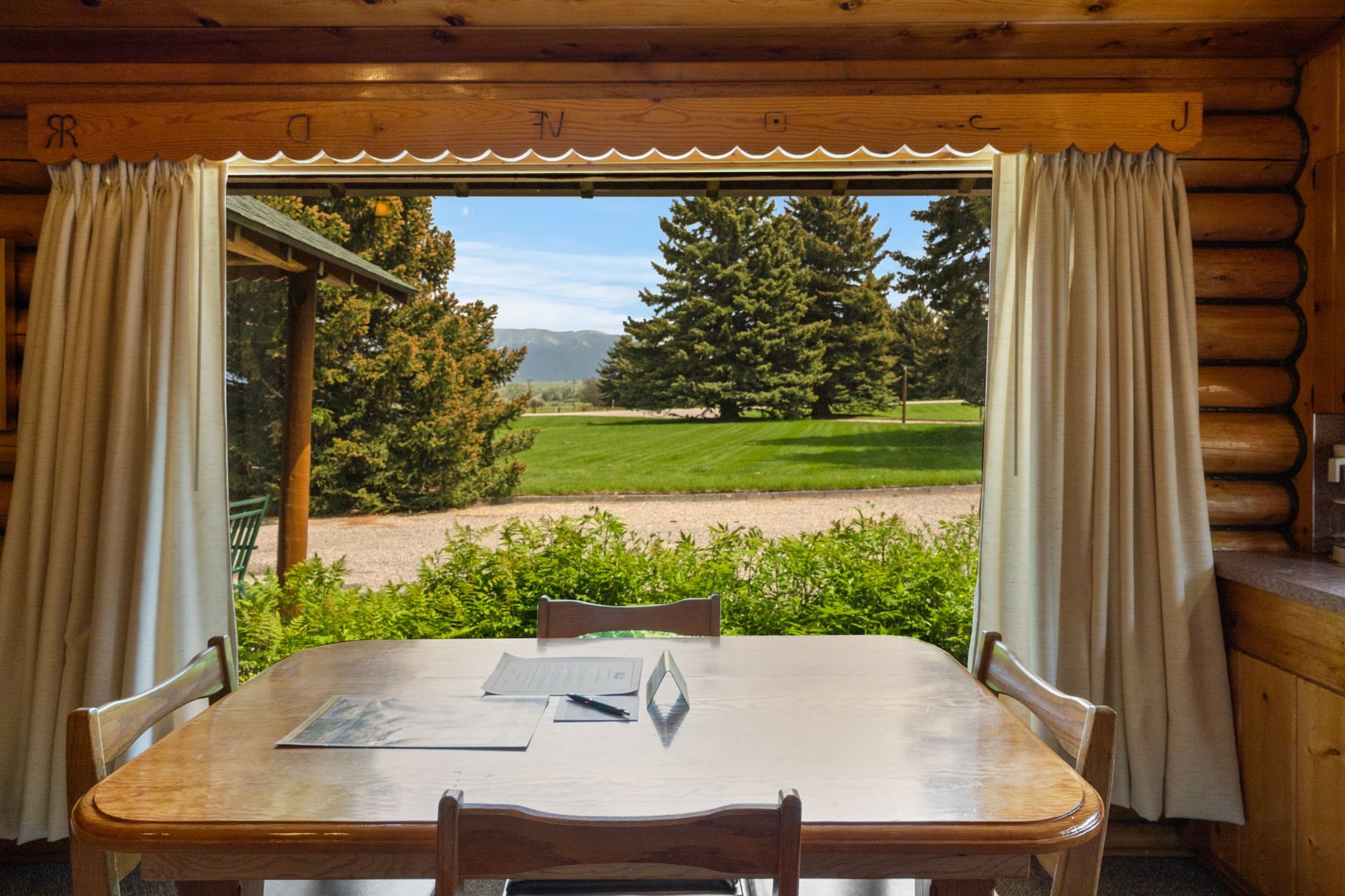 A table and chairs in a log cabin with a view of a field.