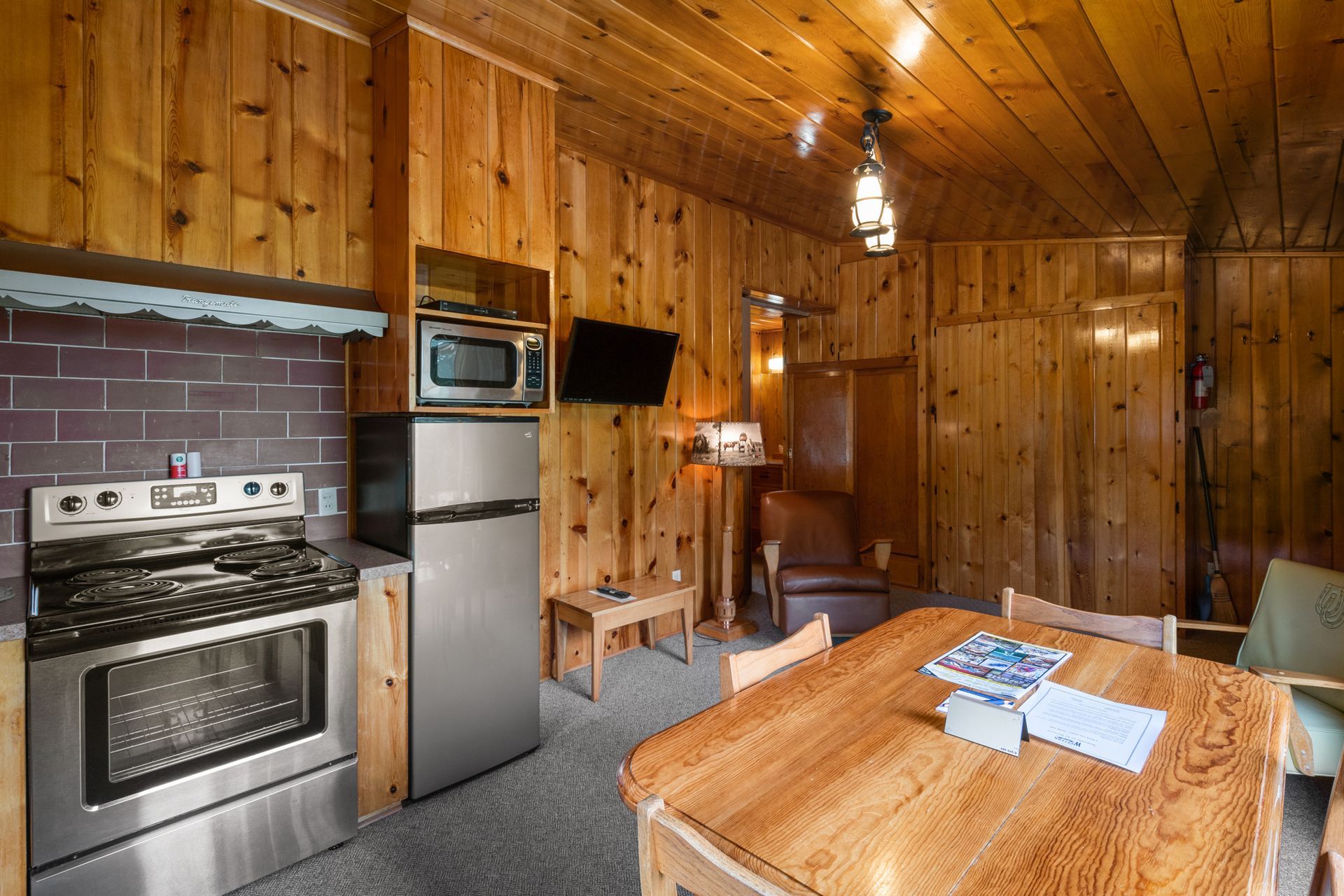 A kitchen with a stove , refrigerator , microwave and table.